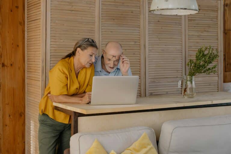 Couple looking at laptop on kitchen counter with bamboo blinds behind them.